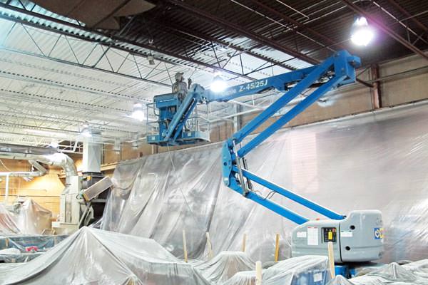 painter spray painting a metal deck ceiling in a factory